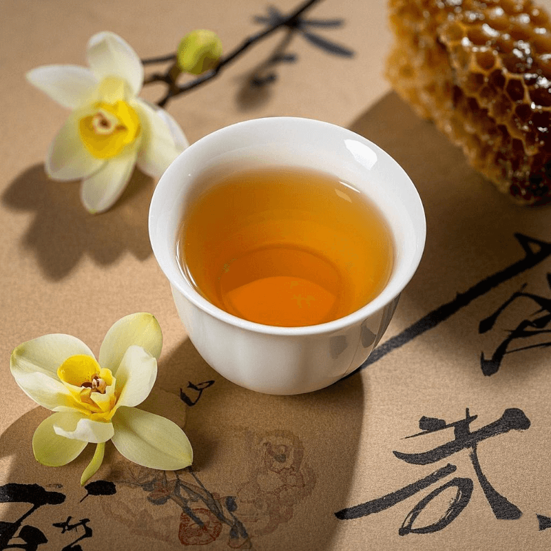 A porcelain cup of Mi Lan Xiang Phoenix Dan Cong oolong tea with golden liquor, surrounded by hints of orchid flowers and honey – highlighting the complex aroma and unique character of this top-rated oolong tea from China